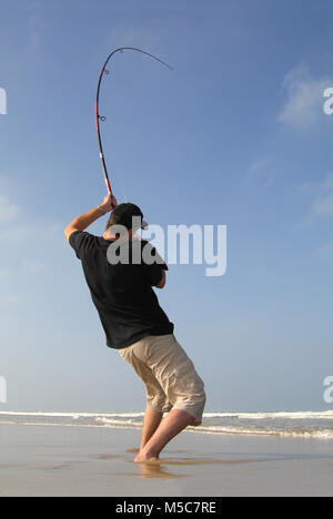 Surf fisherman fighting a fish on a beach, fishing scene. the rod is bending Stock Photo