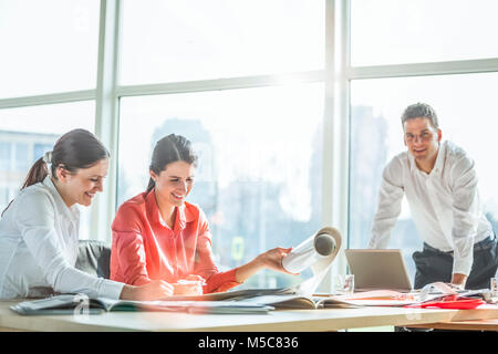 Young architects working on blueprint at desk in office Stock Photo