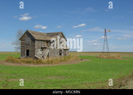 Abandoned farm house in field with broken windmill Stock Photo