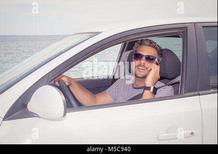 Portrait of young guy making a call with mobile phone while driving Stock Photo