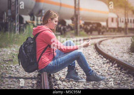 Traveler sitting on rail way and looking at mobile phone Stock Photo