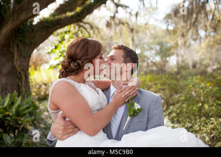 Newly married lovers in garden, groom carrying bride Stock Photo