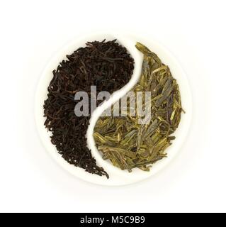 Green tea and black tea in round Yin and Yang white saucer on white background Stock Photo