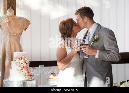 Bride and groom at cake cutting during reception doing wine toast with kiss Stock Photo