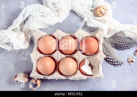 Fresh brown eggs in craft paper tray on a light background with feathers and cloth. Ingredients for Easter cooking. High key header with copy space. Stock Photo