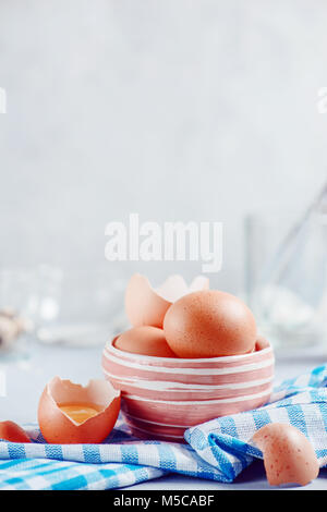 Brown eggs in a ceramic bowl on a light background with milk, flour and ingredients for Easter cooking. High key background with copy space. Stock Photo