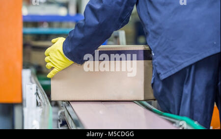 Worker lifting box off production line. Packaging plant with a box being lifted off conveyor belt. Stock Photo