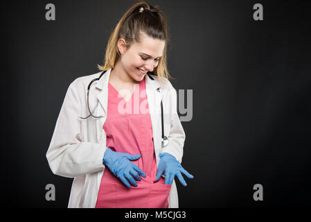 Young doctor portrait  wearing robe looking in her pocket and smiling on black background with copyspace advertising area Stock Photo
