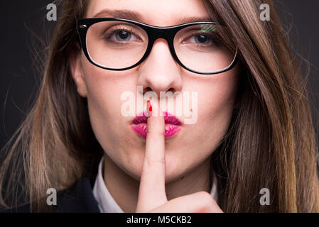 Closeup view of businesswoman shushing a quiet gesture on dark background Stock Photo