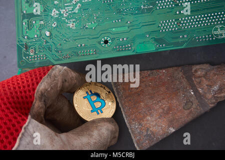 Golden bitcoin lying on the dirty glove, computer components background. Dirty criminal bitcoin or hard diging concept. Stock Photo