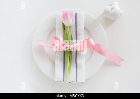 Easter table setting with pink ribbon and tulip on white background. Spring romantic dinner. Top view. Stock Photo