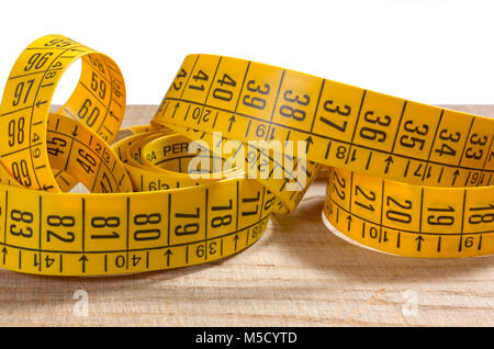 Rolled-up yellow tailor measuring tape on an old wooden surface Stock Photo