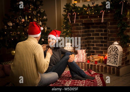Young couple celebrating Christmas when drinking tea at a fireplace Stock Photo