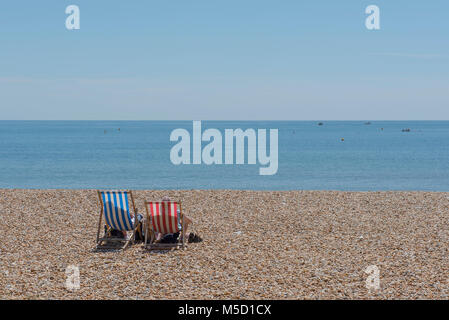 Soaring temperatures on the South Coast of England as Couple relax on traditional striped deckchairs with parasol on a scorching hot day in Lyme Regis Stock Photo