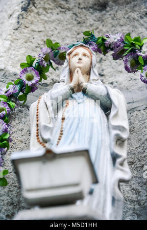 closeup marble sculpture of praying woman against stone and violet flowers garland Stock Photo