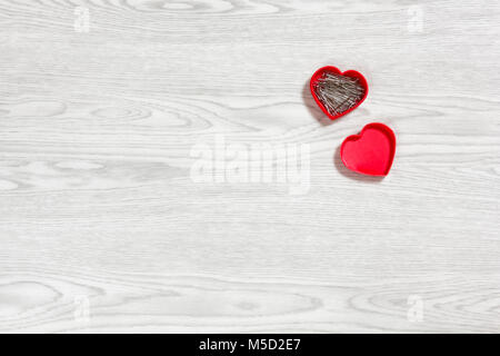 Small red heart-shaped open plastic box full of pins on a white wooden background Stock Photo