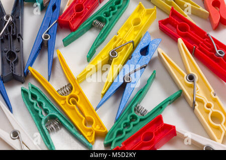 Clothespins of different shapes, sizes and colours scatered across a white background Stock Photo