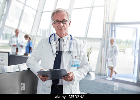 Portrait confident senior male doctor with clipboard in hospital lobby Stock Photo