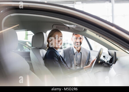 Portrait smiling woman and car salesman sitting in new car at car dealership Stock Photo