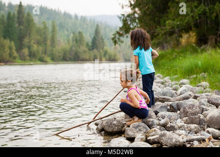 Girl sisters playing with sticks at lakeside Stock Photo