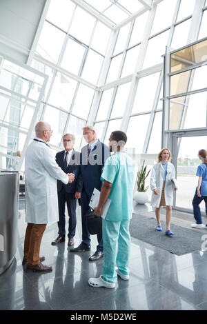 Male surgeon greeting, shaking hands with administrator businessmen in hospital lobby Stock Photo