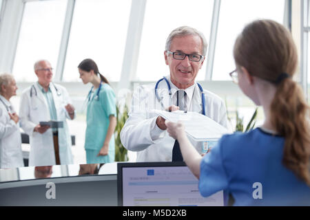 Male doctor handing clipboard to female nurse at hospital nurses station Stock Photo