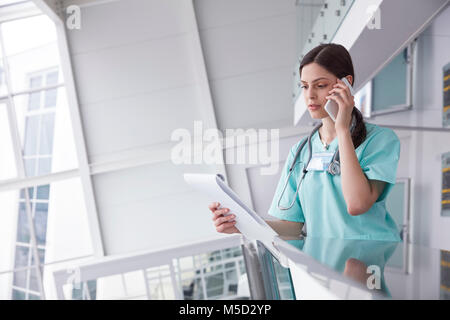 Female nurse with clipboard talking on cell phone in hospital Stock Photo