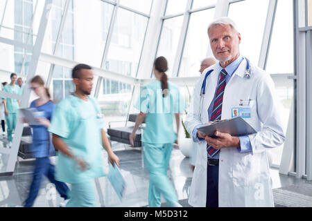 Portrait confident male doctor with clipboard in busy hospital lobby Stock Photo