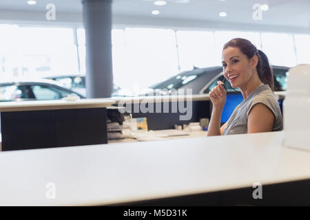 Smiling female receptionist talking on hands-free device telephone in car dealership showroom Stock Photo