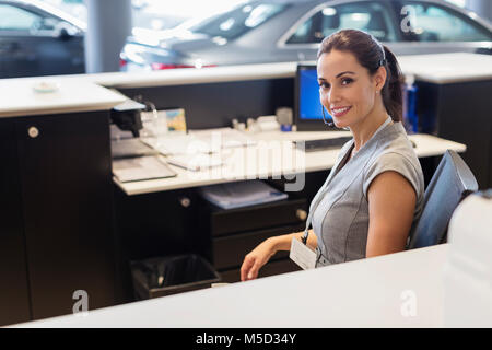 Portrait smiling, confident female receptionist working at desk in car dealership showroom Stock Photo