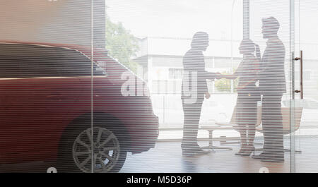 Car salesman shaking hands with couple customers in car dealership showroom Stock Photo