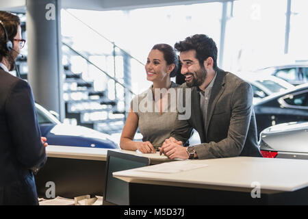 Couple customers talking to receptionist at desk in car dealership showroom Stock Photo