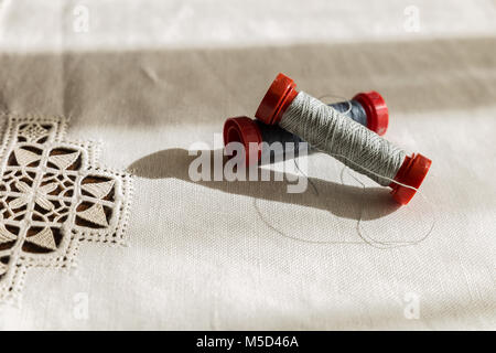 two spools of gray thread on a hand-embroidered tablecloth Stock Photo