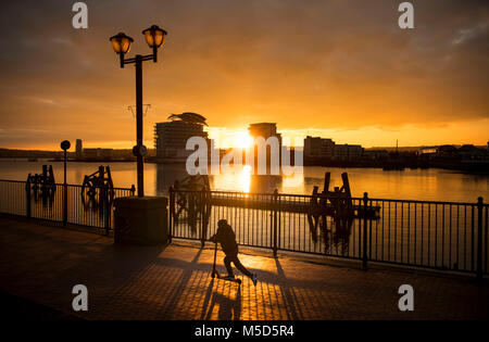 A boy rides a toy scooter at Cardiff Bay at sunset, in Cardiff, South Wales, UK. Stock Photo
