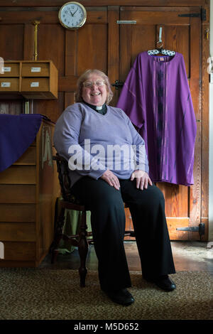 a female vicar sits in her office of a church in her vicars outfit