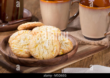 Pile of lemon cookies on a wooden plate with coffee cups in background Stock Photo