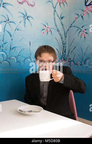a young happy and confident man with down syndrome sits at a table in a cafe Stock Photo