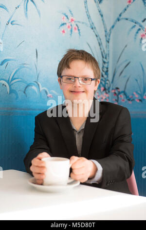 a young happy and confident man with down syndrome sits at a table in a cafe Stock Photo