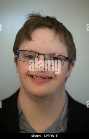 a young man with downs syndrome sits at a table in a cafe drinking coffee Stock Photo