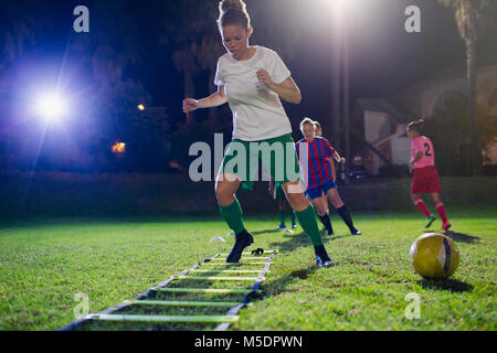 Young female soccer players practicing agility sports drill on field at night Stock Photo
