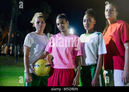 Portrait confident, tough young female soccer team with soccer ball on field at night Stock Photo