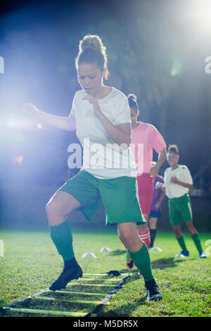 Young female soccer players practicing agility sports drill on field at night Stock Photo