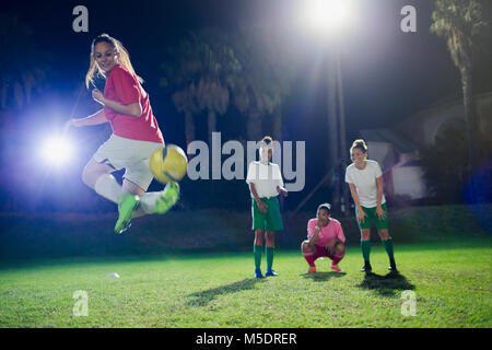 Young female soccer players practicing on field at night, doing back kick Stock Photo