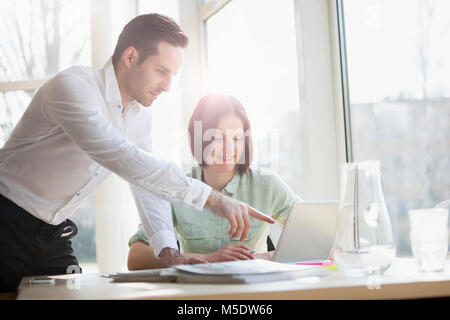 Young businessman showing something to female colleague on laptop at office desk Stock Photo