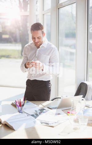 Smiling young businessman text messaging through mobile phone in creative office Stock Photo