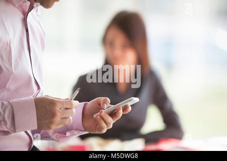 Midsection side view of businessman using cell phone with female colleague in background at office Stock Photo