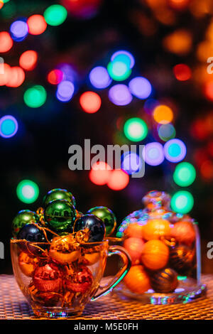 New-year small multicolored balls in a glass cup on a background of girilland lights in blur Stock Photo