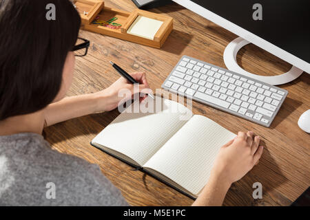 Close-up Of A Businesswoman Writing On Checker Note Book With A Pen At Workplace Stock Photo
