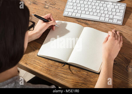 Close-up Of A Businesswoman Writing On Checker Note Book With A Pen At Workplace Stock Photo