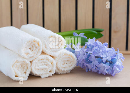 Beige bath towels on wooden background and a fresh violet hyacinth. Spa concept. Stock Photo